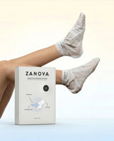 Model with feet raised wearing Zanova plastic collagen foot masks, beside the Zanova Ultimate Trio Hydrating Foot Mask box